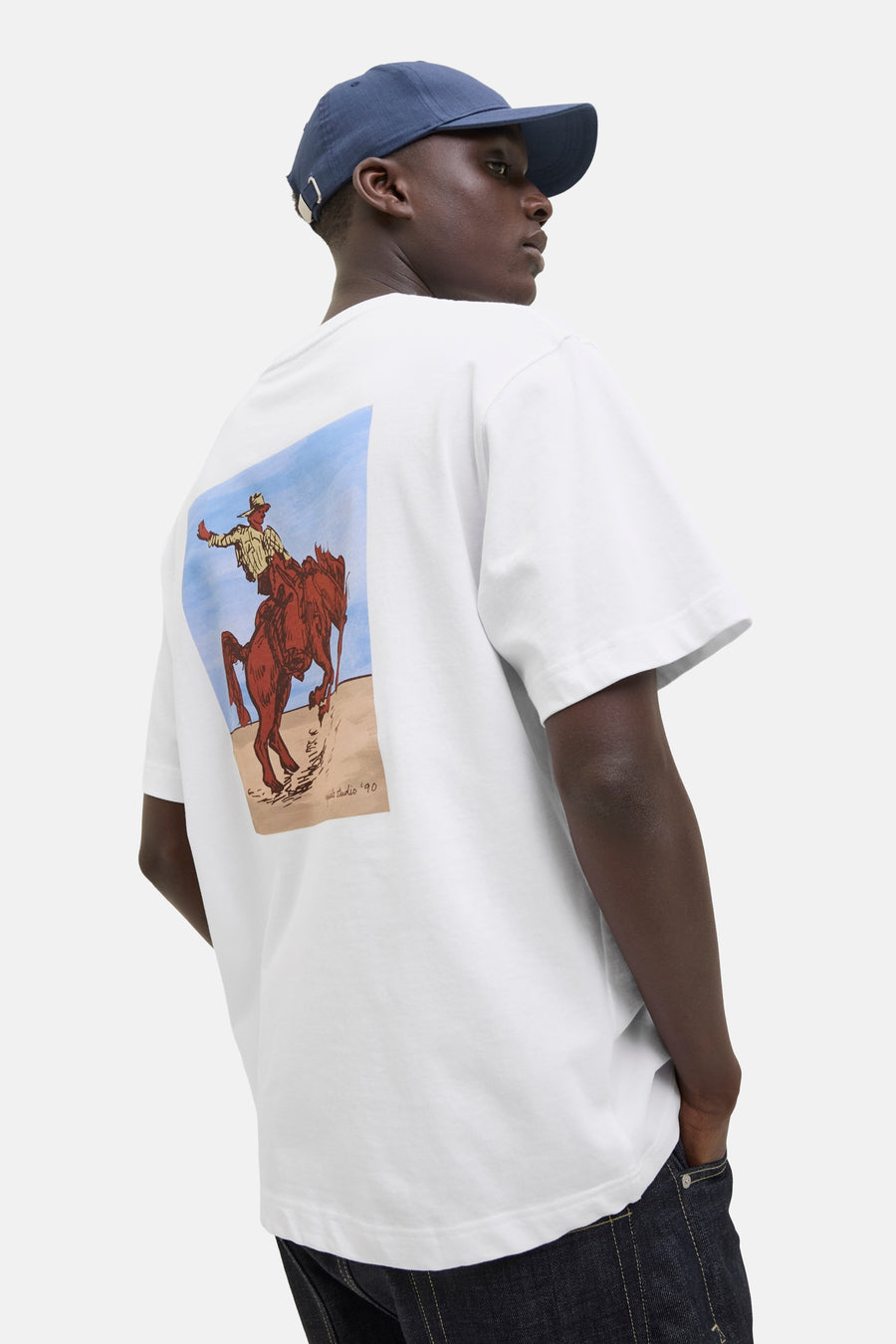Wit T-shirt met korte mouwen van ORIGINALS BY JACK & JONES, met een cowboy print op de rug, gecombineerd met een donkerblauwe pet en jeans.
