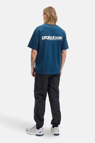 Blauw T-shirt met korte mouwen van CORE BY JACK & JONES, achterkant zichtbaar, gecombineerd met een zwarte trainingsbroek met witte streep en grijze sneakers.