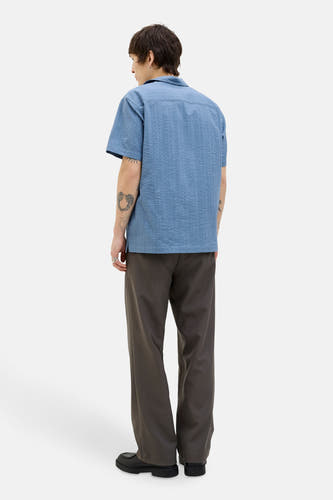 Chemise bleue à manches courtes de PREMIUM BLUE par JACK & JONES, avec une subtile texture, portée avec un pantalon foncé et des chaussures noires.