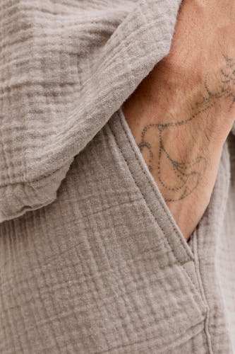 Bruine short van ORIGINALS BY JACK & JONES, met een textuurstof en een hand in de zak met tatoeage.
