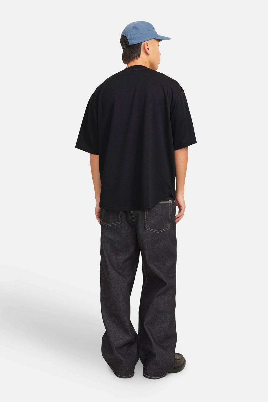 Achterkant van een man in zwarte kleding en een blauwe pet.