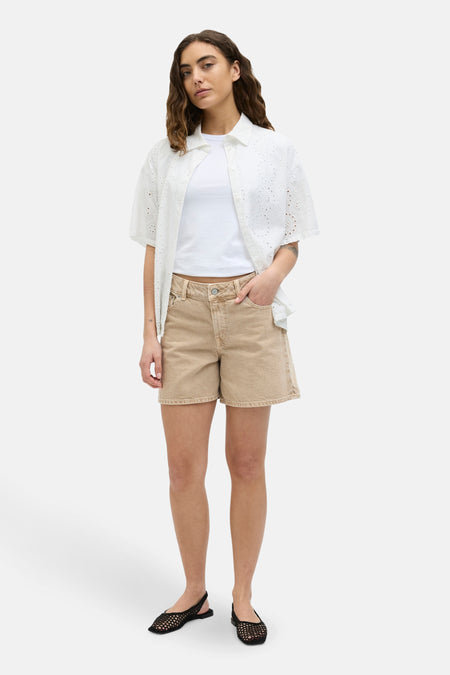 Short beige de JJXX, associé à un T-shirt blanc et un chemisier blanc ouvert avec des détails en bordure.