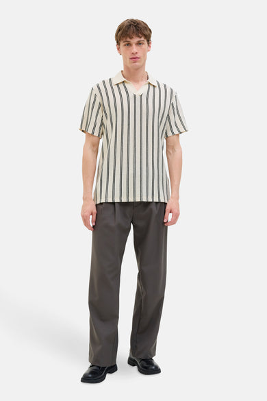 Polo beige à manches courtes de PREMIUM BLUE par JACK & JONES, avec des rayures noires verticales, associé à un pantalon gris foncé et des chaussures noires.