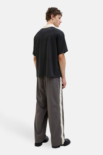 Polo noir à manches courtes de CORE BY JACK & JONES, avec un col beige, porté avec un pantalon gris et une bande blanche.