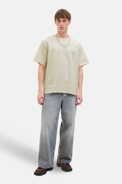 Man met beige T-shirt, blauwe jeans en bruine schoenen.