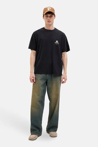 T-shirt noir à manches courtes d'ORIGINALS BY JACK & JONES, avec une petite impression sur la poitrine, porté avec un chapeau marron et des jeans vintage.
