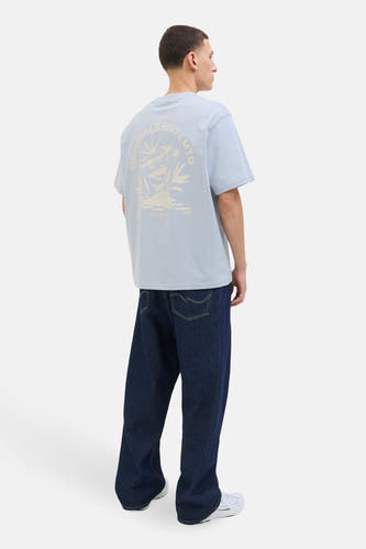 T-shirt bleu à manches courtes d'ORIGINALS BY JACK & JONES, avec une impression sur le dos, associé à des jeans foncés et des baskets blanches.