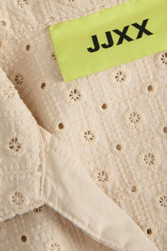Beige mouwloze blouse van JJXX, met een open bloemenpatroon en een lichtgekleurd label.
