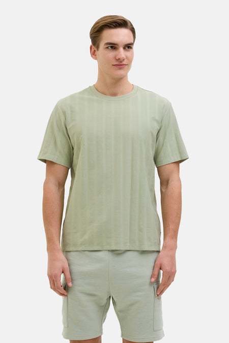 Groen T-shirt met korte mouwen van JJREBEL, met een verticaal gestreept textuurpatroon, gecombineerd met shorts.

