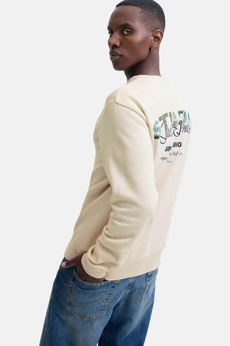 Gilet beige de CORE par JACK & JONES, avec logo sur le dos et porté avec des jeans bleus.