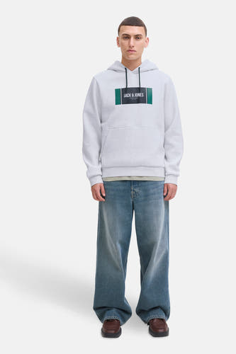 Grijze sweater met kap van CORE BY JACK & JONES, met logo op de borst, gedragen met wijde jeans en bruine schoenen.
