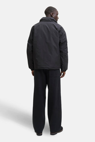 Zwarte korte jas van CORE BY JACK & JONES, gezien van achteren, met wijde zwarte broek en oorbellen.