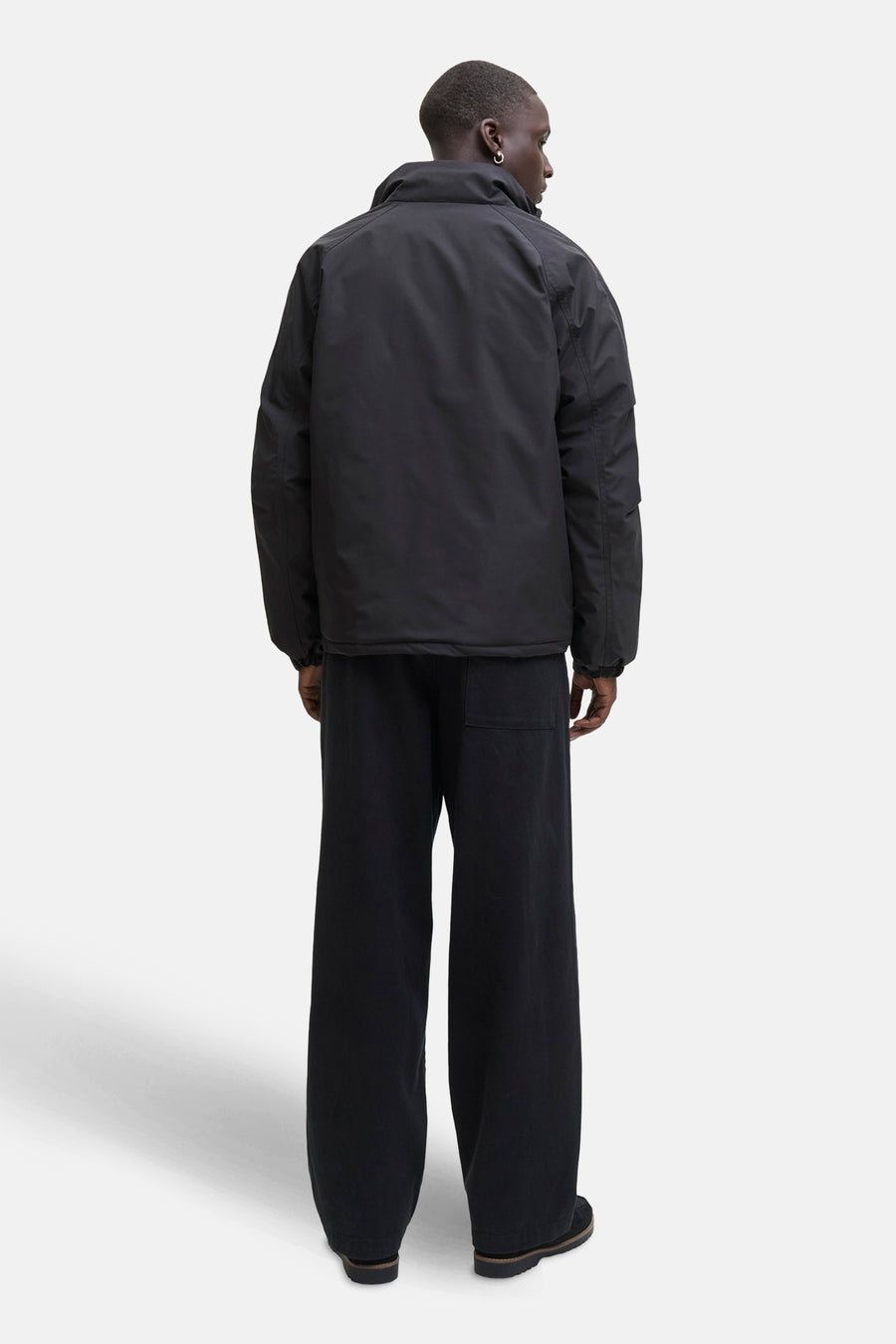 Zwarte korte jas van CORE BY JACK & JONES, gezien van achteren, met wijde zwarte broek en oorbellen.