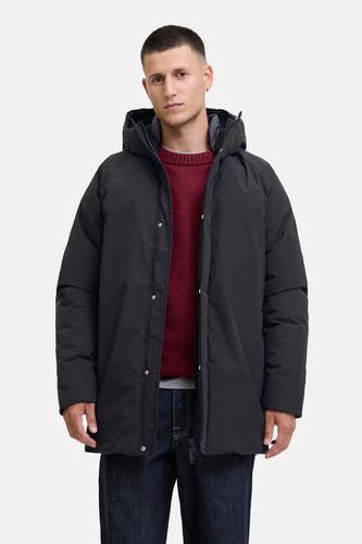 Zwarte lange jas van ORIGINALS BY JACK & JONES, met capuchon en gedragen over een rode trui en donkere jeans.