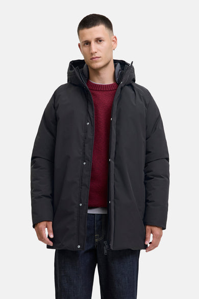 Manteau long noir d'ORIGINALS BY JACK & JONES, avec capuche et porté sur un pull rouge et des jeans foncés.
