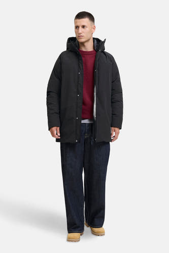 Zwarte lange jas van ORIGINALS BY JACK & JONES, met capuchon, gedragen met een rode trui en wijde jeans.

