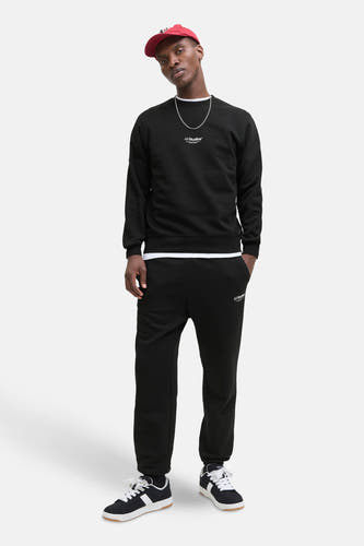 Gilet noir de CORE BY JACK & JONES, avec impression textuelle et porté avec une chaîne argentée et un chapeau rouge.