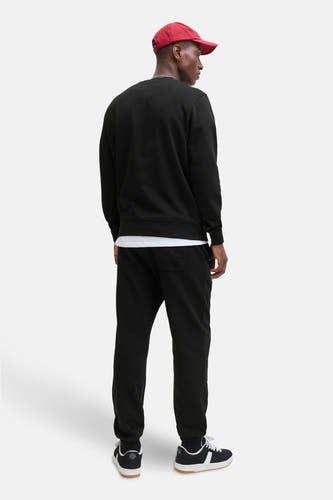 Pull-over noir de CORE BY JACK & JONES, avec un col rond, associé à un bonnet rouge et une jogging noire.