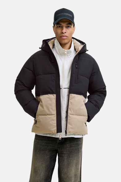Manteau court noir de CORE BY JACK & JONES, avec une bande beige en bas et le modèle porte un chapeau et des jeans gris.