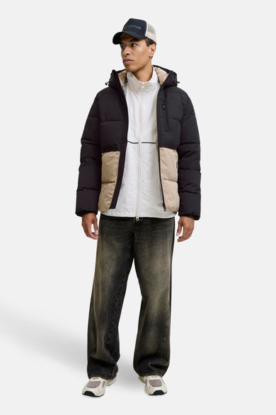 Manteau court noir de CORE BY JACK & JONES, avec des détails beige et porté avec un pull blanc et un jean.