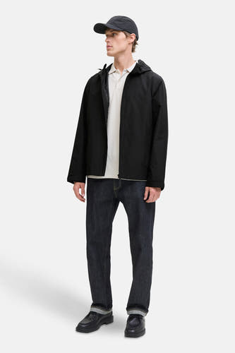 Zwarte korte jas van ORIGINALS BY JACK & JONES, met capuchon, gecombineerd met een polo, jeans en zwarte schoenen.