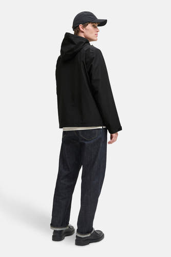 Zwarte korte jas van ORIGINALS BY JACK & JONES, met capuchon en donkere jeans met opgerolde pijpen.
