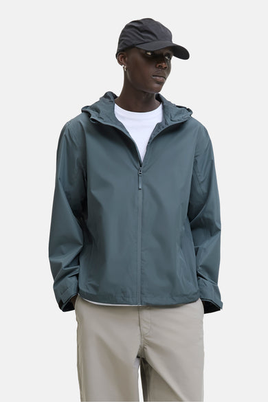 Grijze korte jas van ORIGINALS BY JACK & JONES, met capuchon en een witte T-shirt en beige broek.
