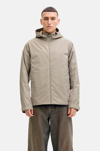 Beige jas van ORIGINALS BY JACK & JONES, met capuchon en rits, gedragen over een donkerblauw shirt en wijde jeans.