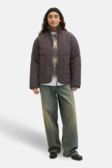Bruine korte jas van JJXX, met een gewatteerd patroon en gedragen over een trui en wijde jeans.
