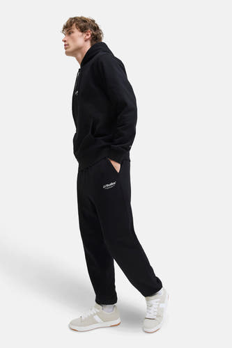 Zwarte joggingbroek van JACK & JONES JEANS INTELLIGENCE, met logo en steekzak, gecombineerd met witte sneakers en sokken.