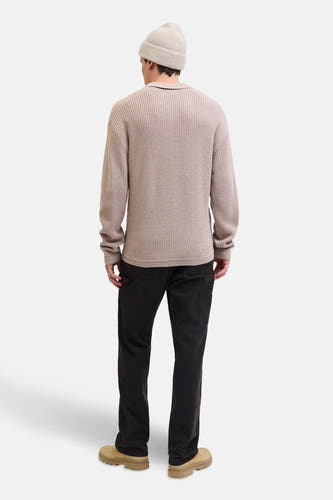 Gilet V-hals beige de PREMIUM par JACK & JONES, porté avec un bonnet, un pantalon foncé et des bottes en cuir suédois.
