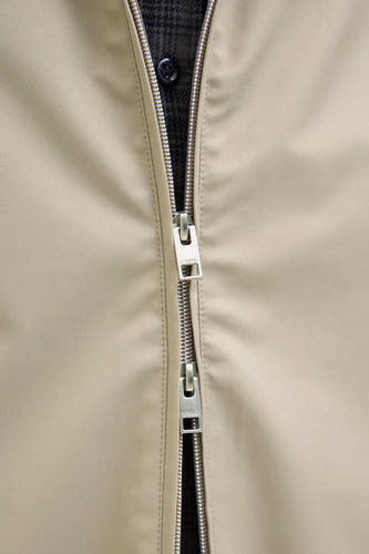 Ecru manteau court de JJREBEL, avec une fermeture éclair argentée et une blouse à carreaux partiellement visible.
