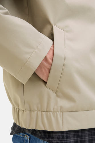 Mauve manteau court de JJREBEL, avec la main dans la poche, porté sur un chemisier à carreaux et des jeans bleus.