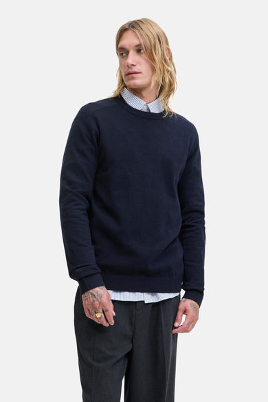 Blauwe trui met ronde hals van PREMIUM by JACK & JONES, gedragen over een gestreept overhemd en met grijze pantalon.