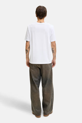 Wit T-shirt met korte mouwen van ORIGINALS BY JACK & JONES, met zichtbare tatoeages en wijde bruine broek.
