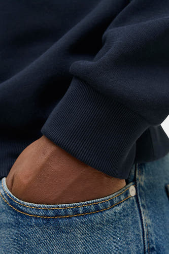 Pull-over bleu d'ORIGINALS BY JACK & JONES, avec des bordures côtelées et une main dans la poche de jeans.