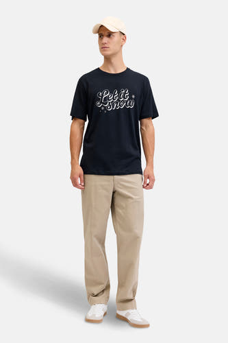 Donkerblauw T-shirt met korte mouwen van ORIGINALS BY JACK & JONES, met een 'Let it snow' print en gedragen met een beige broek en witte sneakers.