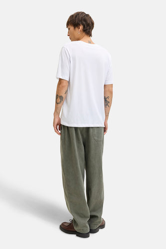 Achterkant van een man in een wit T-shirt, groene broek en bruine schoenen.