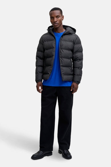 Manteau court noir de CORE BY JACK & JONES, avec capuche, associé à un t-shirt bleu et un pantalon noir.