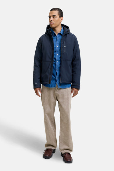 Korte blauwe jas van PREMIUM BLUE by JACK & JONES, gedragen met een denim overhemd en beige broek.