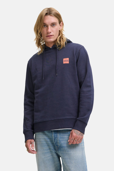 Blauwe sweater met kap van ORIGINALS BY JACK & JONES, met oranje logo-patch en lichtblauwe jeans.