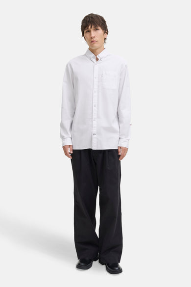 Chemise blanche à manches longues de PREMIUM by JACK & JONES, avec poche poitrine et portée avec un pantalon noir et des chaussures.