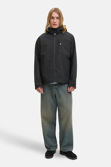 Manteau court noir de CORE BY JACK & JONES, avec capuche, associé à des jeans larges et des mocassins.