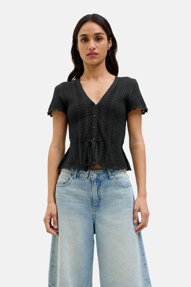 Pull noir JJXX, à manches courtes, avec une fermeture à boutons et une ceinture élastique, associé à un pantalon de denim large.