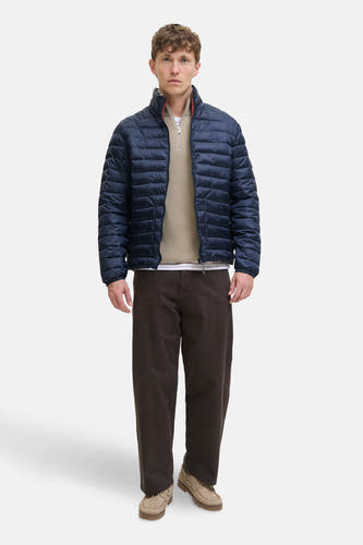 Korte blauwe jas van PREMIUM BLUE by JACK & JONES, met rits en gedragen over een beige trui en bruine broek.
