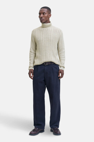 Beige trui met rolkraag van PREMIUM BLUE by JACK & JONES, met kabelpatroon en gedragen met marineblauwe pantalon en bruine schoenen.
