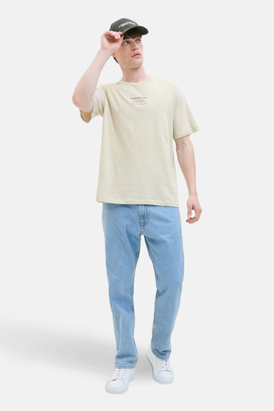 T-shirt écru à manches courtes de JJREBEL, porté avec un chapeau sombre, des jeans bleus et des baskets blanches.