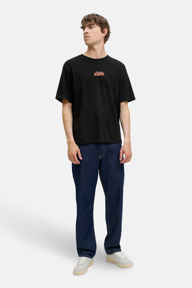 T-shirt noir à manches courtes de JJREBEL, avec un logo texte orange sur la poitrine, associé à des jeans bleu marine.