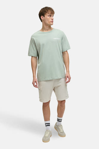 Groen T-shirt met korte mouwen van JJREBEL, gedragen met beige shorts en lage sneakers met sokken.