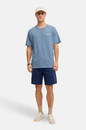 Blauw T-shirt met korte mouwen van JJREBEL, met tekstprint, gedragen met donkerblauwe shorts, beige sokken en sneakers.